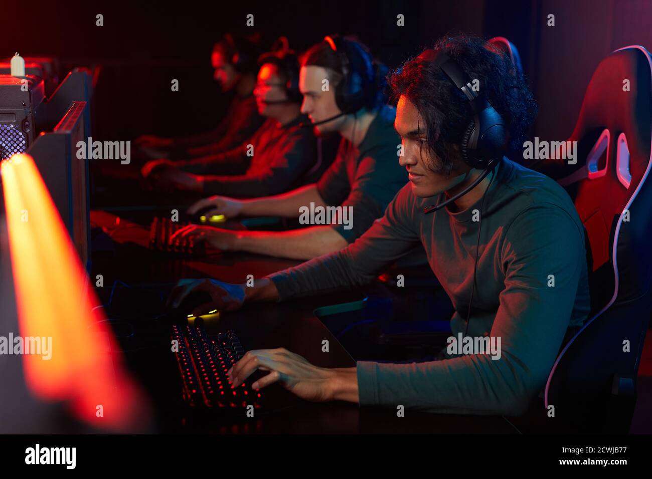 Gruppo di ragazzi in cuffia seduti al tavolo di fronte al computer e di giocare giochi per computer in club Foto Stock