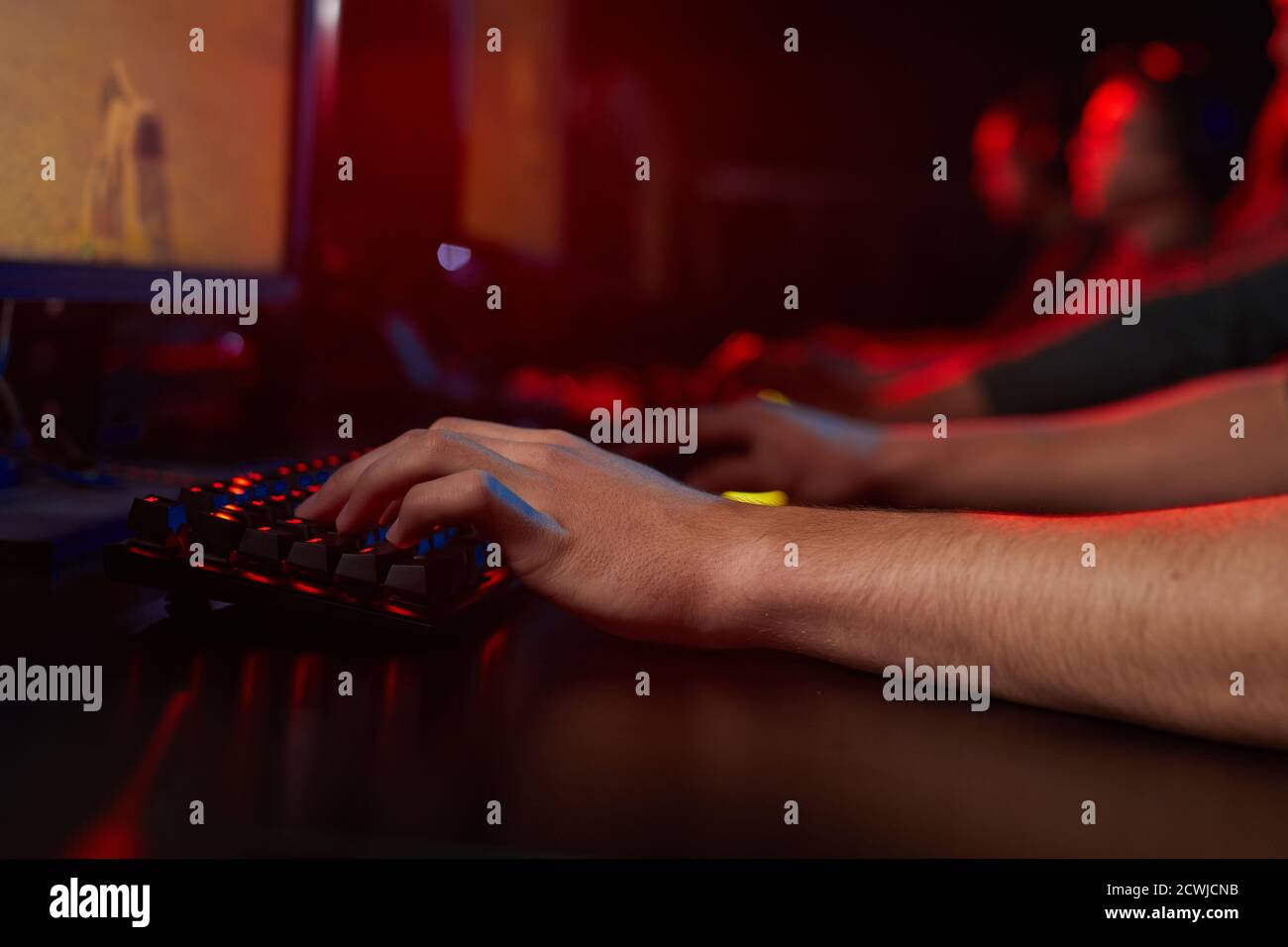 Primo piano del giovane seduto al tavolo e digitando sulla tastiera del computer in una stanza buia Foto Stock