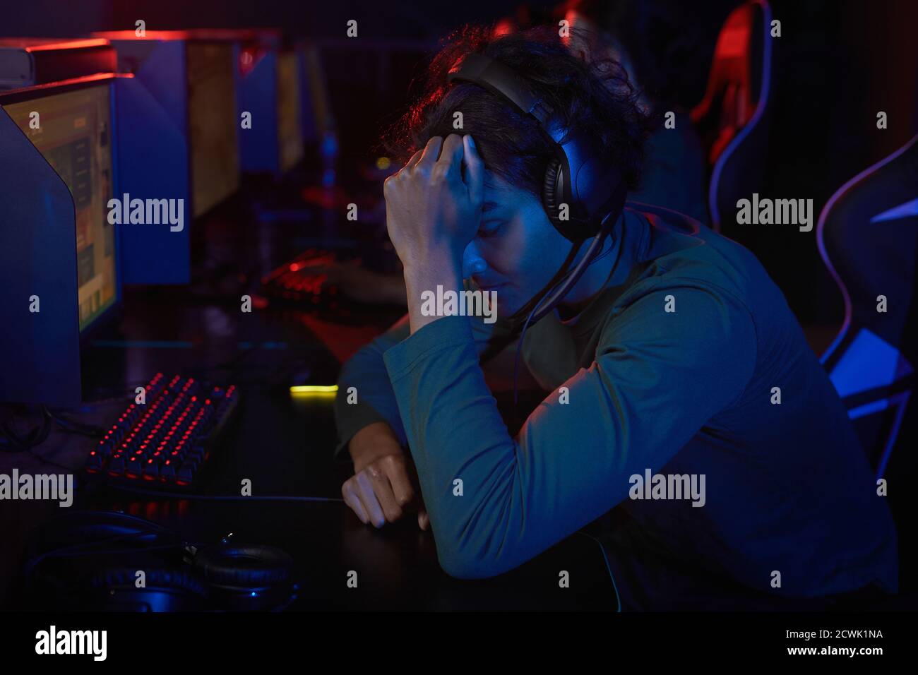 Sviluppatore stanco nelle cuffie seduto al tavolo davanti di computer e tenendo la testa ha un mal di testa Foto Stock