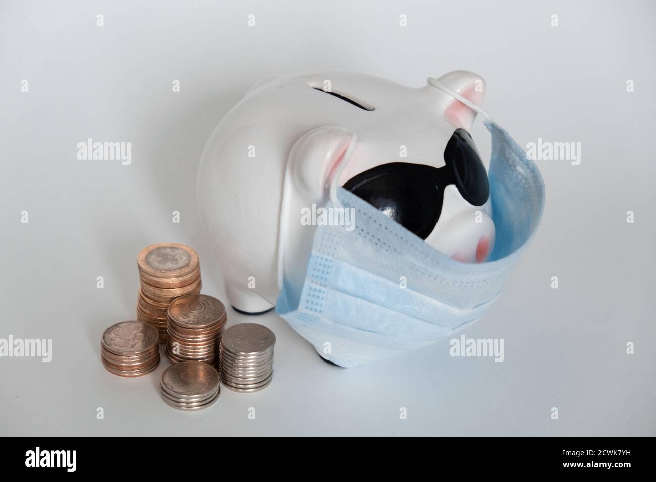 pericolo di risparmio finanziario dovuto a un virus pandemico. porcellino banca in una maschera su sfondo bianco. monete Foto Stock