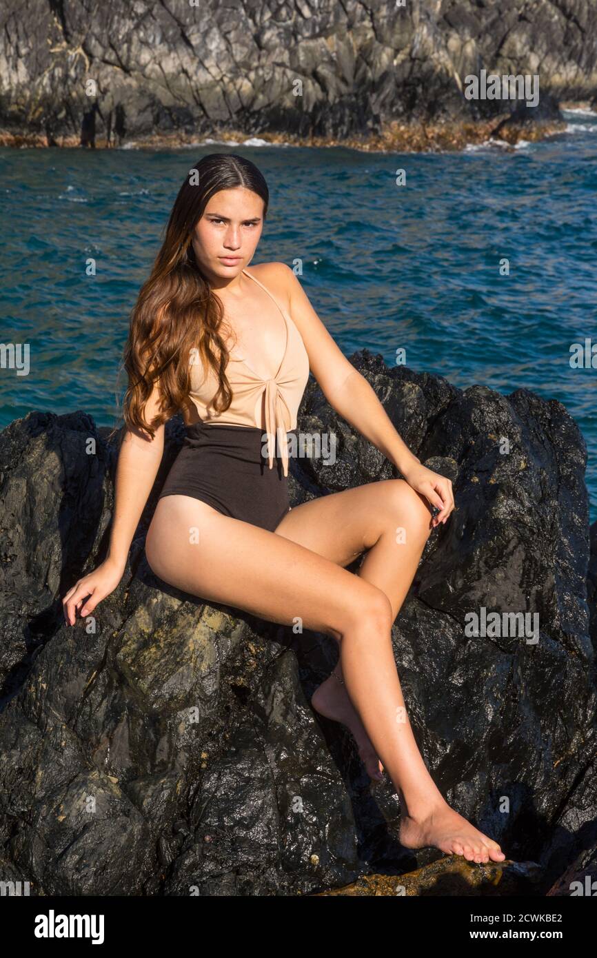 Una donna si siede al sole su una roccia costiera spiaggia e guarda la macchina fotografica a Los Roques Venezuela Foto Stock