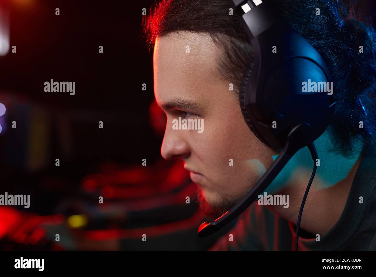 Primo piano di un giocatore serio in cuffie che si concentra sul suo computer gioco seduto al tavolo Foto Stock