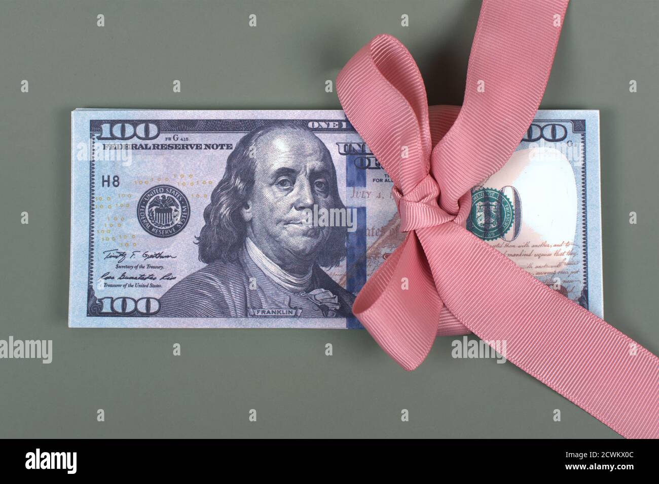 Centinaia di dollari legati con arco rosa su sfondo grigio. Denaro, regalo avvolto in fiocco rosa e nastro, valuta americana, contanti, successo aziendale, bonus Foto Stock
