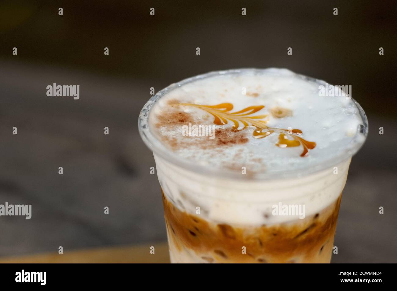 Il caffè ghiacciato con latte cremoso in un bicchiere di plastica è su un tavolo, fuoco selettivo, latte art Foto Stock