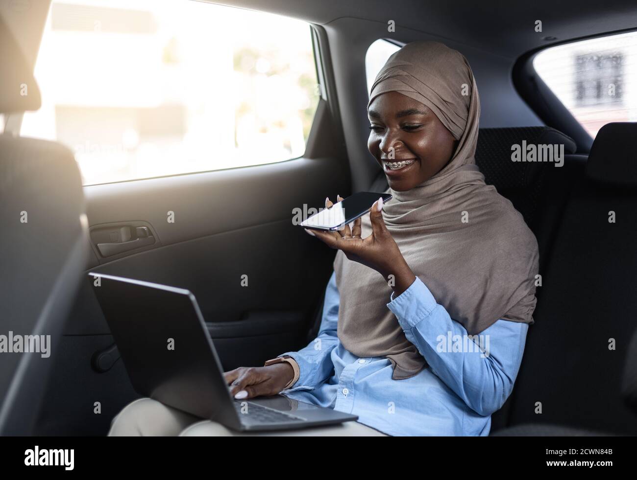 Black Muslim Business Woman registrazione messaggio audio con smartphone in Auto Foto Stock