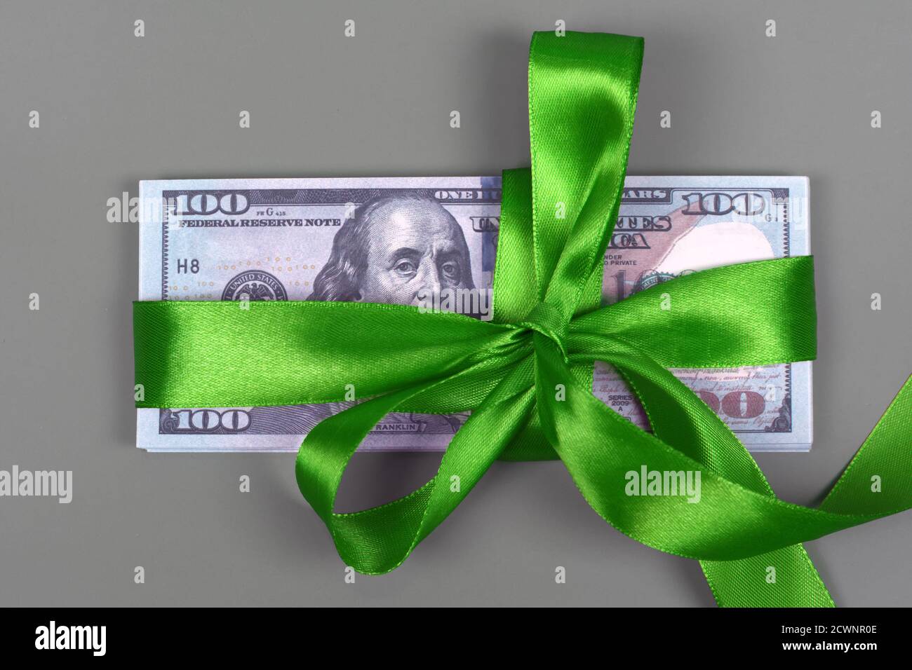 Centinaia di dollari legati con arco verde su sfondo grigio. Denaro, regalo avvolto in fiocco verde e nastro, valuta americana, contanti, successo aziendale, bonus Foto Stock