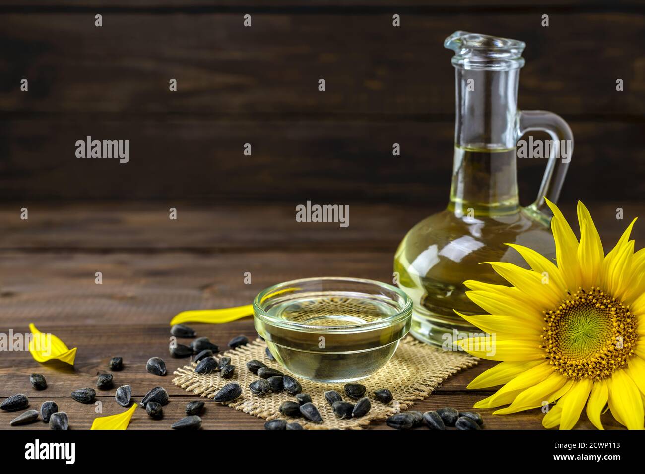 Olio di girasole in bottiglia e semi di girasole vicino a fiori di girasole freschi su sfondo di legno con spazio per la copia del testo. Foto Stock