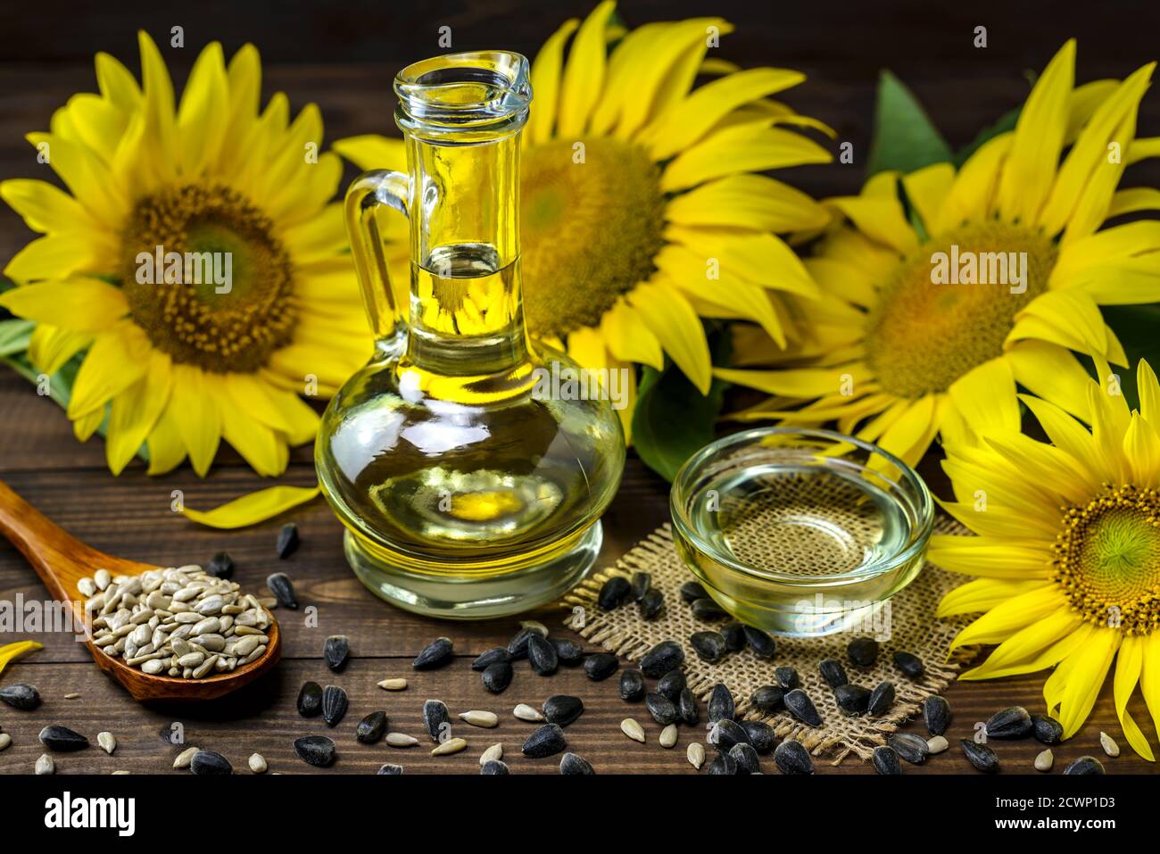 Olio di girasole in bottiglia e semi di girasole vicino a fiori di girasole freschi su sfondo di legno. Messa a fuoco selettiva. Foto Stock
