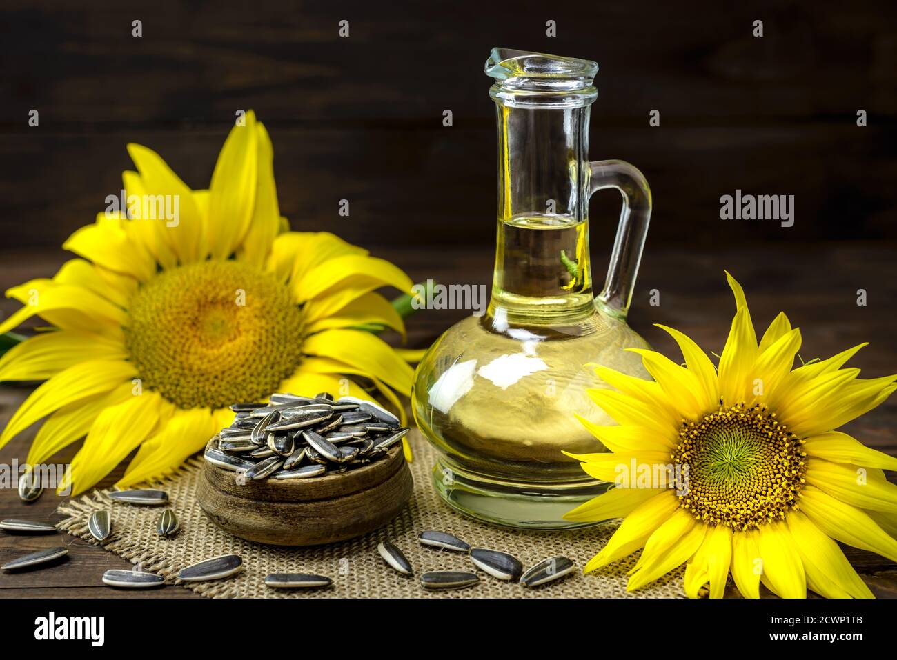 Olio di girasole in una bottiglia e semi di girasole in una ciotola vicino al fiore di girasole fresco su un tavolo di legno. Foto Stock