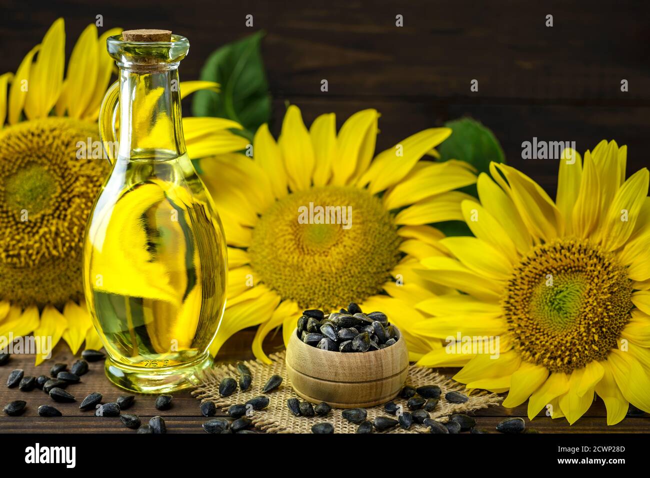Olio di girasole in una bottiglia e semi di girasole in una ciotola vicino al fiore di girasole fresco su un tavolo di legno con spazio di copia per il testo. Foto Stock