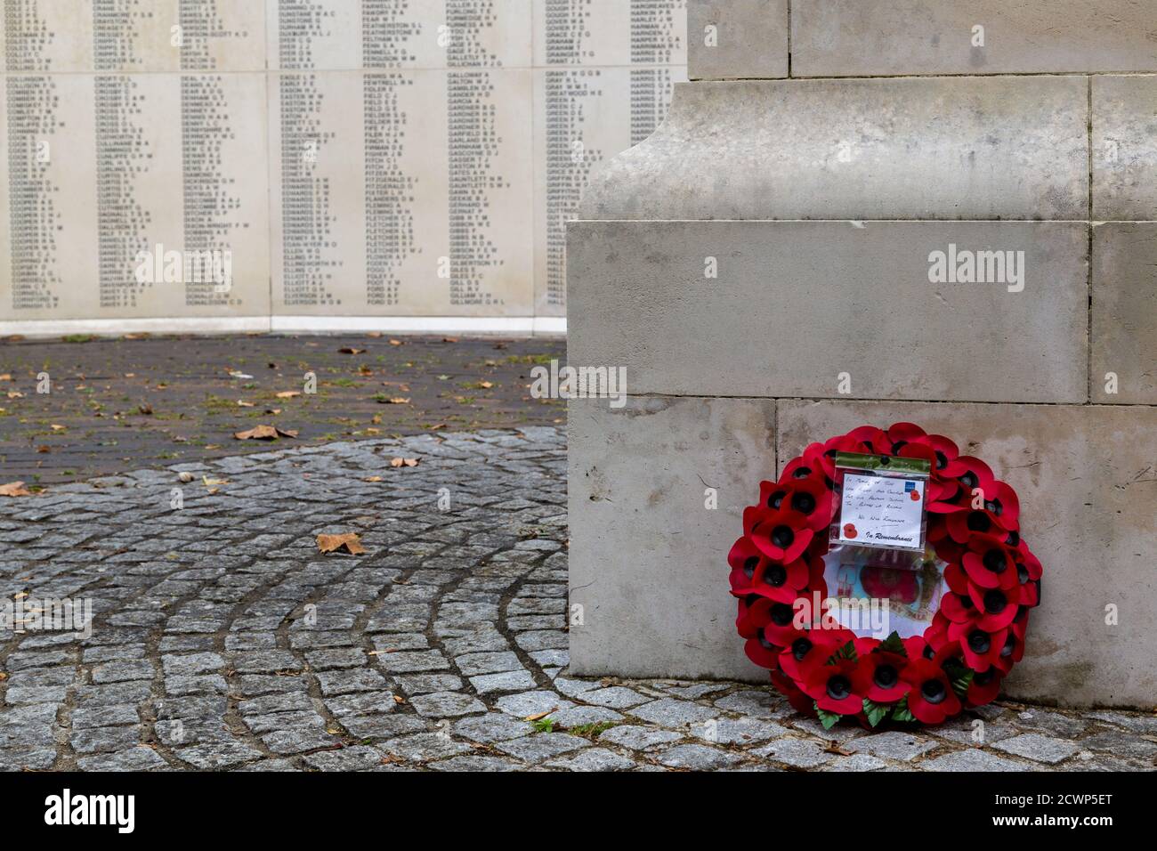 Una sola corona rossa di papavero contro un memoriale di guerra con i nomi di coloro che sono morti nelle guerre mondiali sfocato sullo sfondo Foto Stock
