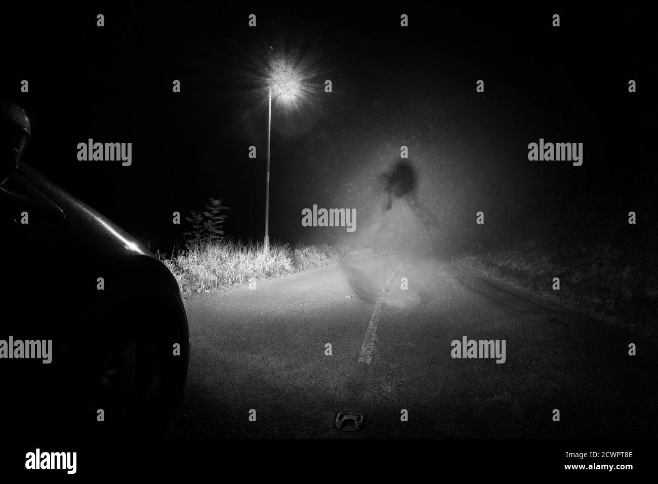Un fantasma spooky di una donna nella strada sotto una singola luce di strada in campagna. Illuminato dai fari dell'auto di notte. Con un grunge, vintage, vecchio e. Foto Stock