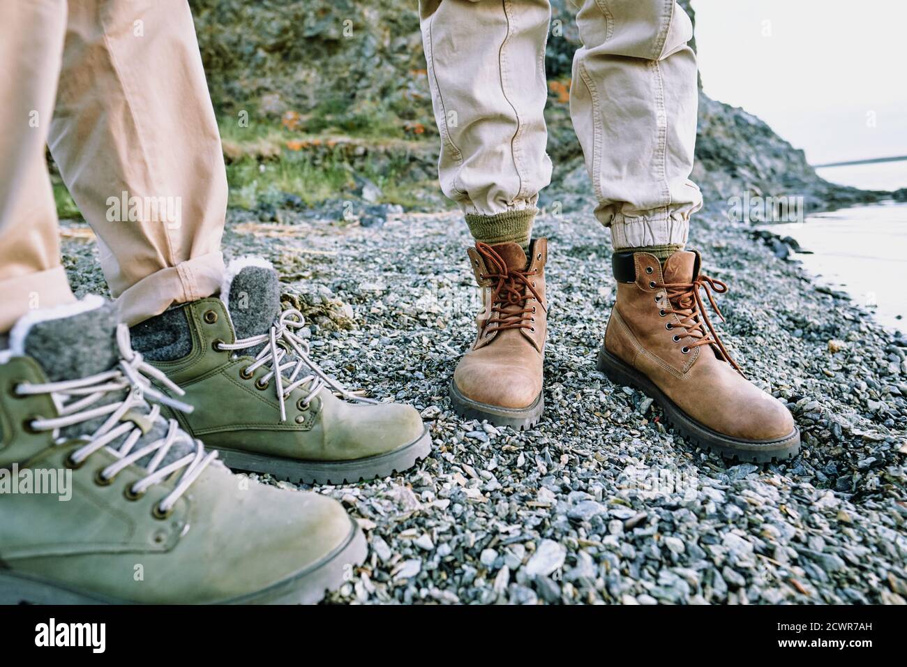 Primo piano di una coppia irriconoscibile in piedi in comodi stivali da trekking ciottoli vicino all'acqua Foto Stock
