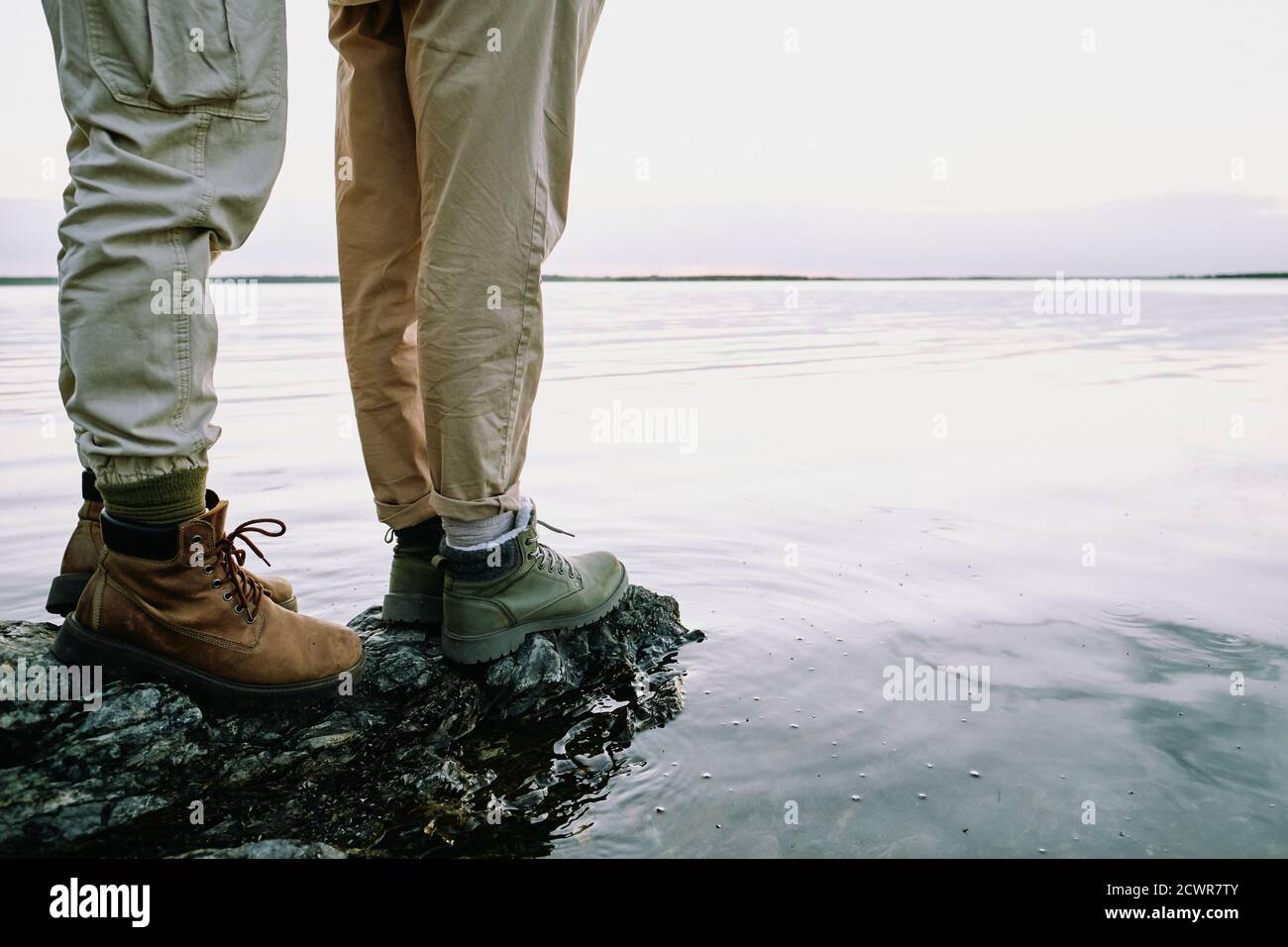 Primo piano di una coppia irriconoscibile in stivali da trekking in piedi sulla roccia e contemplando il paesaggio acquatico Foto Stock