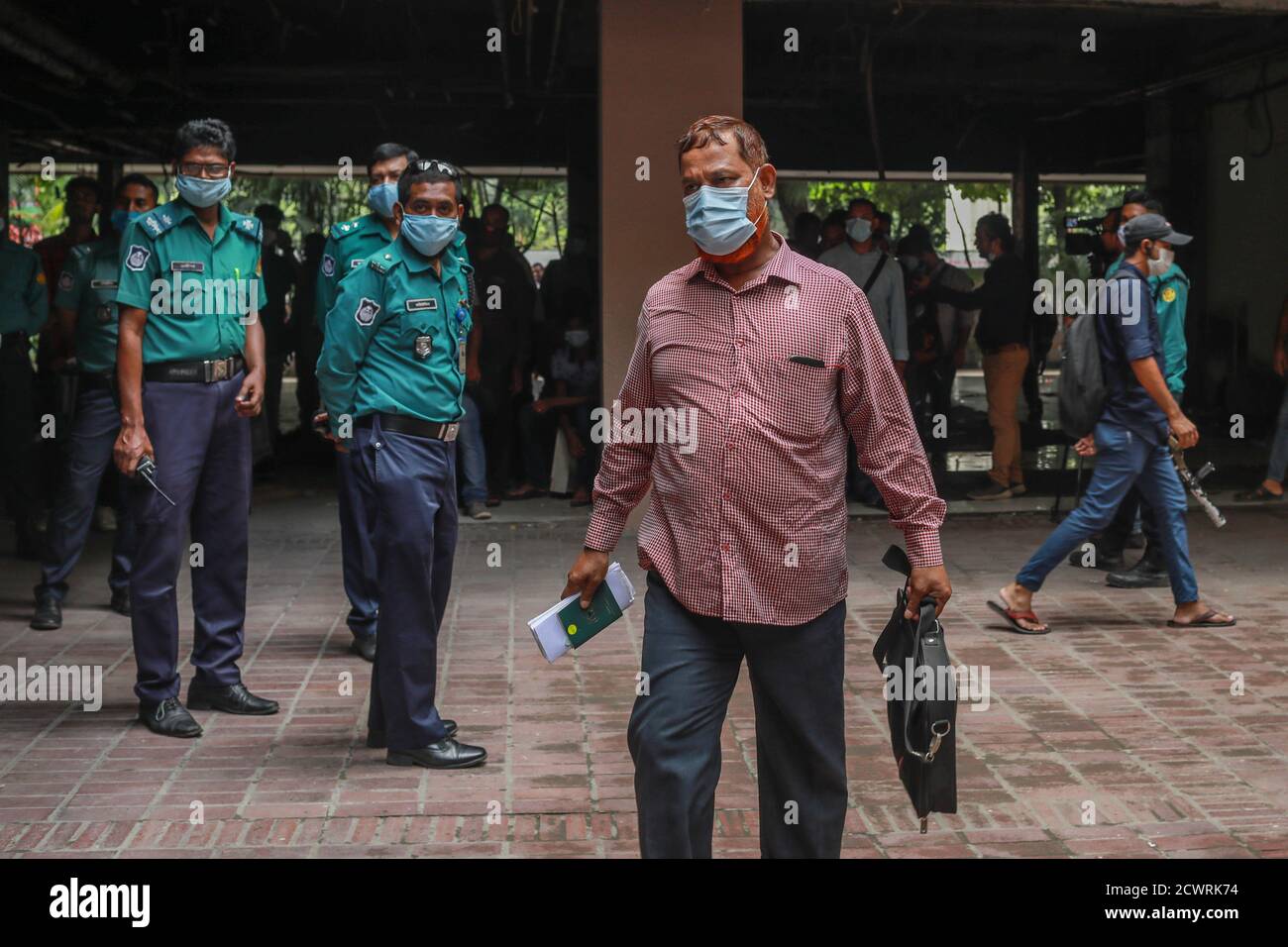 Gli agenti di polizia che indossano maschere facciali che sono venuti a monitorare la situazione guardano a un uomo che ha ottenuto il suo biglietto aereo di ritorno nelle sue mani.centinaia di lavoratori migranti del Bangladesh sono attualmente in attesa presso gli uffici delle compagnie aeree dell'Arabia Saudita all'hotel Pacific Sonargaon per ritirare i biglietti di ritorno al loro lavoro destinazioni in tempo. Foto Stock