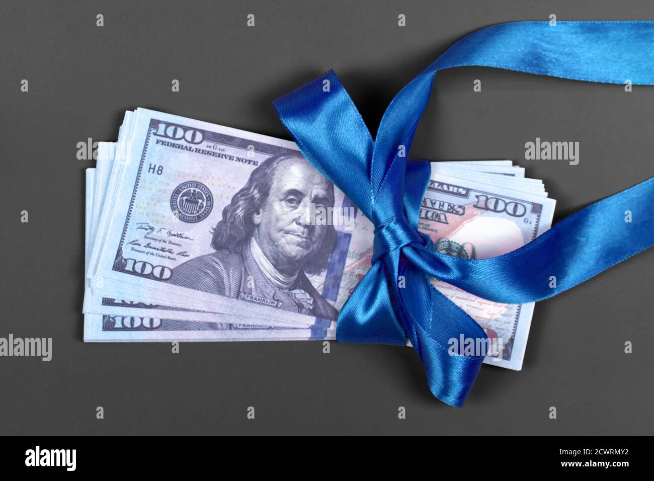 Soldi come concetto di regalo, vittoria o indennità, le fatture di cento dollari su sfondo grigio. Pila di 100 dollari fatture è legato con nastro blu con arco. Foto Stock