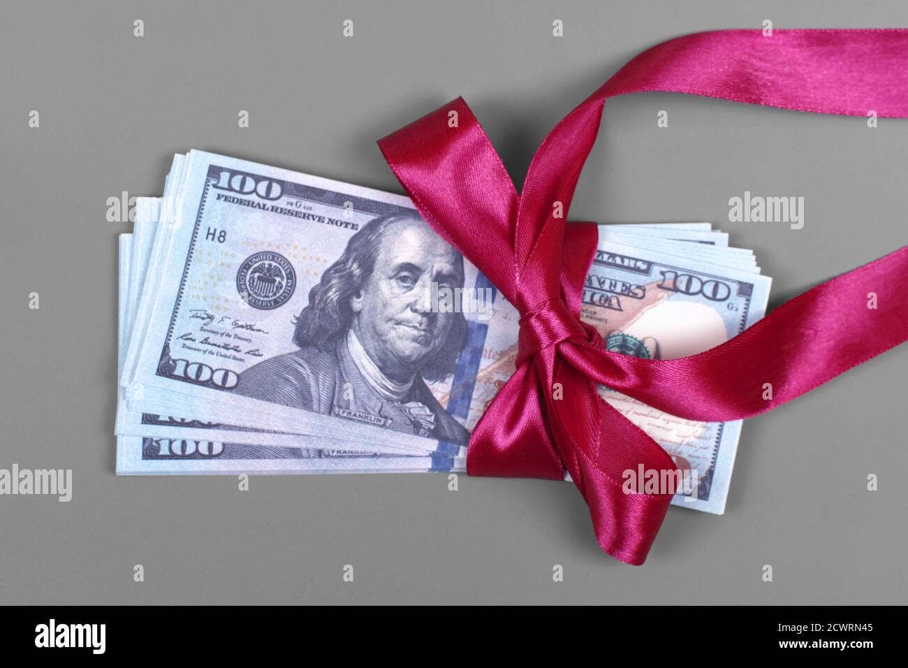 Soldi come concetto di regalo, vittoria o indennità, le fatture di cento dollari su sfondo grigio. Pila di 100 dollari di fatture è legato con nastro rosso con arco. Foto Stock