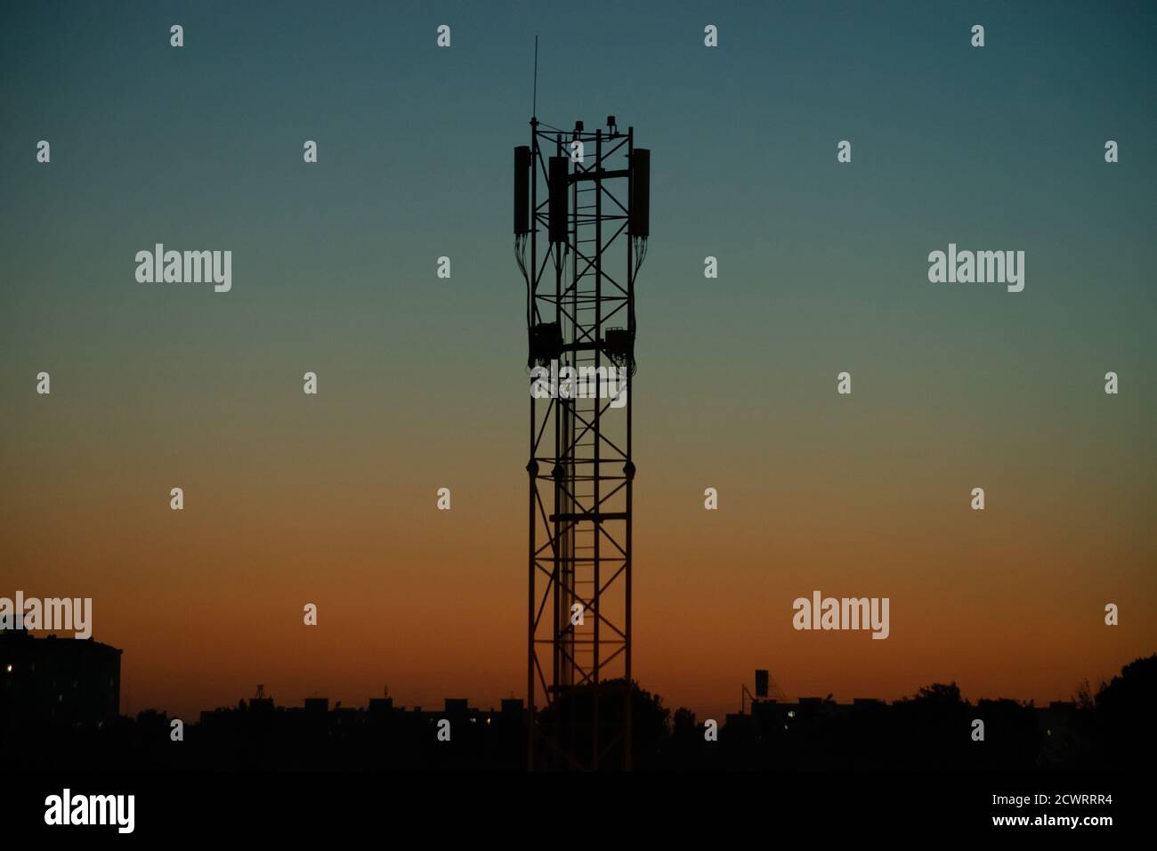 Silhouette della torre di comunicazione dell'antenna dell'operatore mobile contro sfondo del cielo arancione-blu sera Foto Stock
