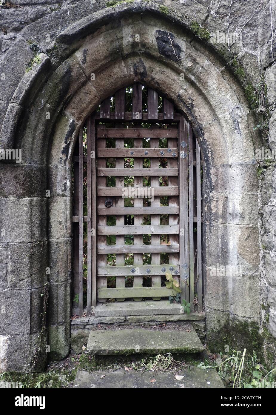 Una porta in pietra arcuata in stile gotico romanico a Whalley Abbey, Lancashire, UK. Con porta a griglia interna a graticcio in legno. Sebbene la maggior parte degli edifici siano stati demoliti, rimangono ancora un certo numero di muri e caratteristiche e le fondamenta di altre parti sono state scavate e lasciate in vista. L'abbazia chiuse nel 1537 durante lo scioglimento dei monasteri nello stesso anno in cui l'abate Giovanni Paslew fu giustiziato per alto tradimento da parte sua nel pellegrinaggio di grazie degli eventi dell'anno precedente Foto Stock