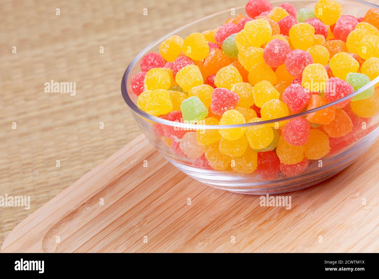 La gomma di frutta cade in una ciotola di vetro su sfondo di legno Foto Stock