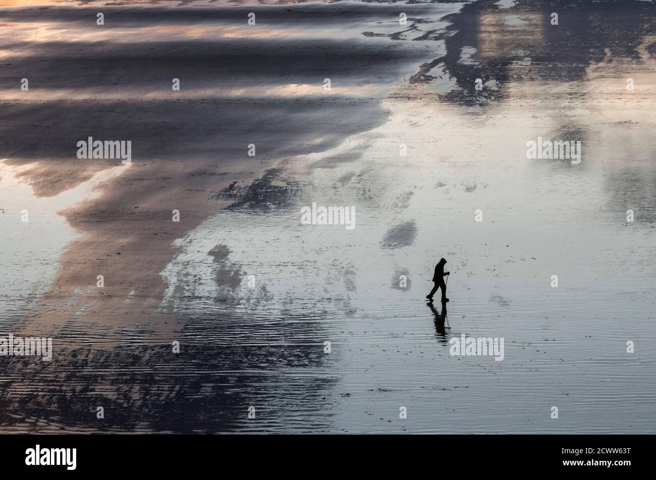 Uomo con bastone che cammina su una spiaggia vuota in basso marea Foto Stock