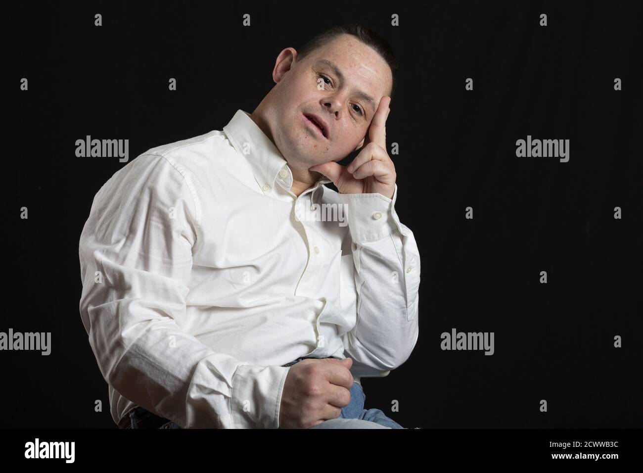 L'uomo ispanico adulto con la sindrome di Down posa in studio fotografico con camicia bianca e jeans Foto Stock