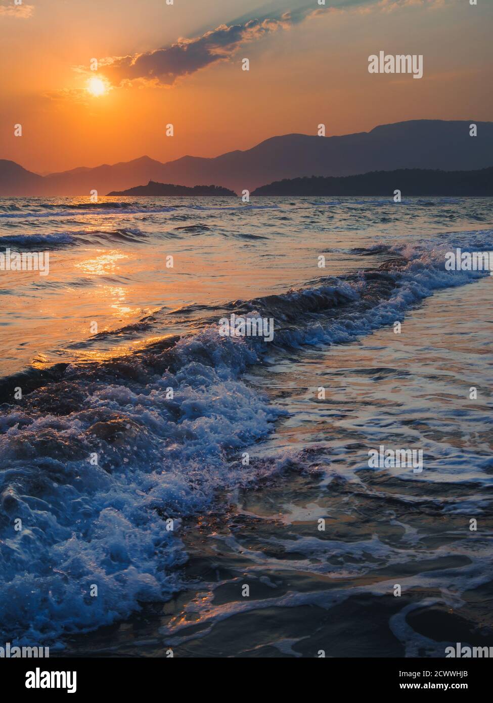 Colorata scena di onde che si infrangono sulla spiaggia di Iztuzu al tramonto con le montagne all'orizzonte e le silhouette del sole che tramonta. Foto Stock