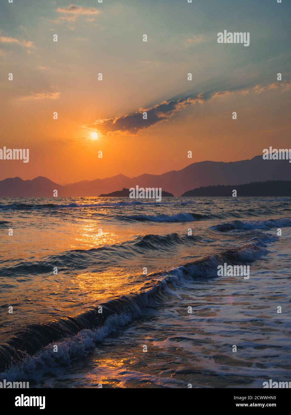 Colorata scena di onde che si infrangono sulla spiaggia di Iztuzu al tramonto con le montagne all'orizzonte e le silhouette del sole che tramonta. Foto Stock