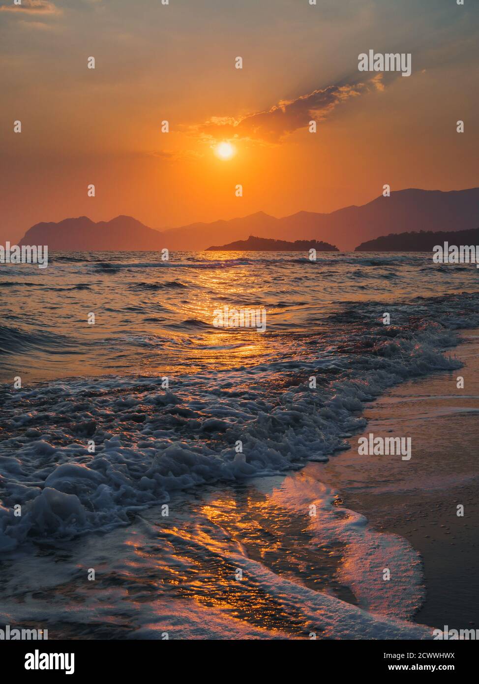 Colorata scena di onde che si infrangono sulla spiaggia di Iztuzu al tramonto con le montagne all'orizzonte e le silhouette del sole che tramonta. Foto Stock