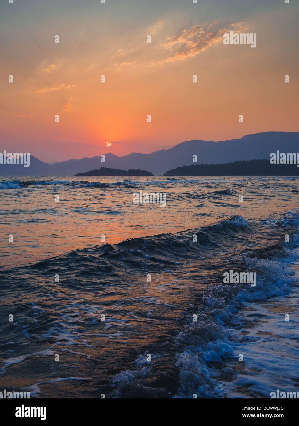 Colorata scena di onde che si infrangono sulla spiaggia di Iztuzu al tramonto con le montagne all'orizzonte e le silhouette del sole che tramonta. Foto Stock