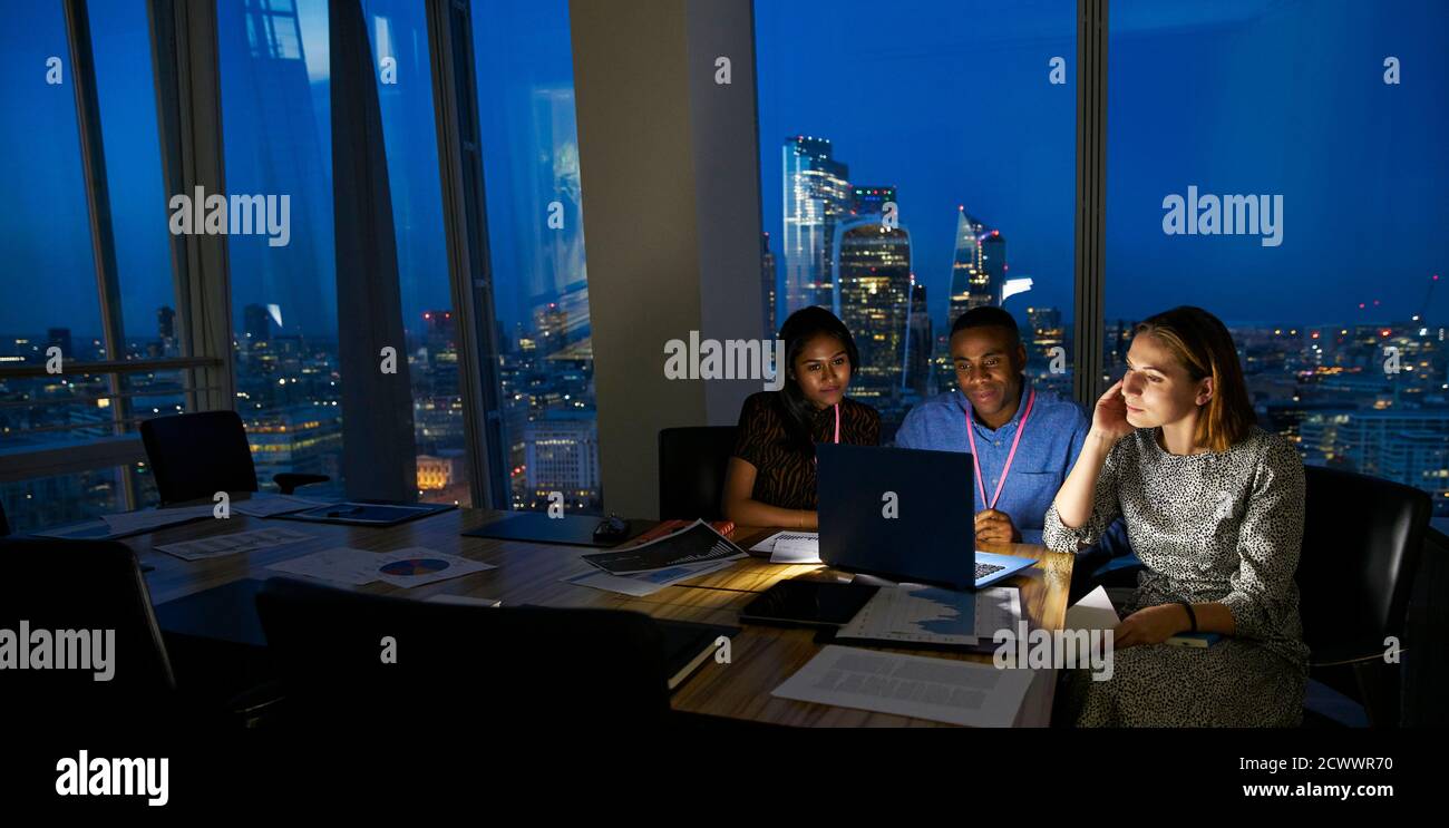 Gli uomini d'affari lavorano fino a tardi con un computer portatile nella sala conferenze di alta altezza Foto Stock