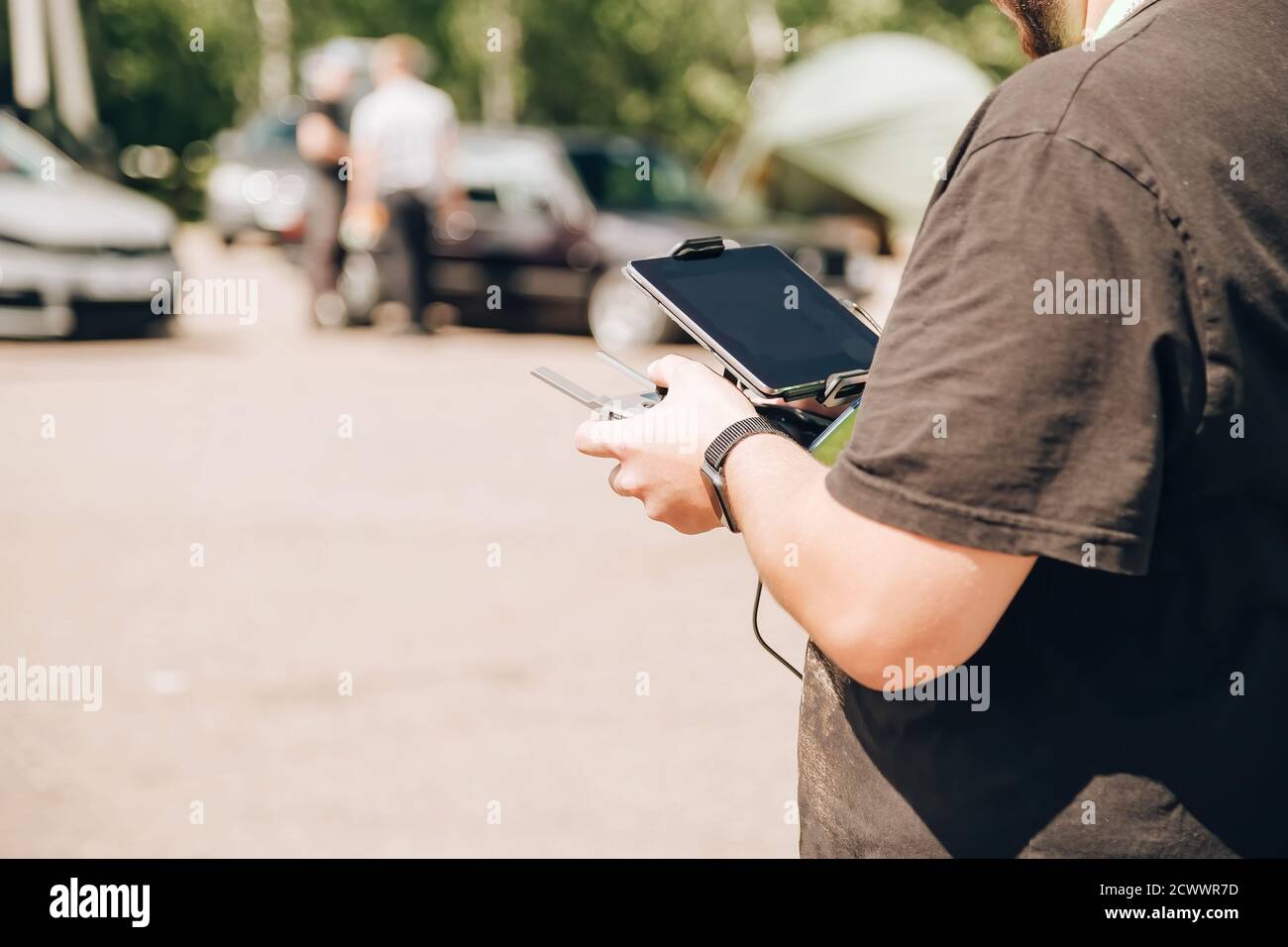 Un uomo nero controlla un drone utilizzando un telecomando e un tablet. È in piedi in un parcheggio auto Foto Stock