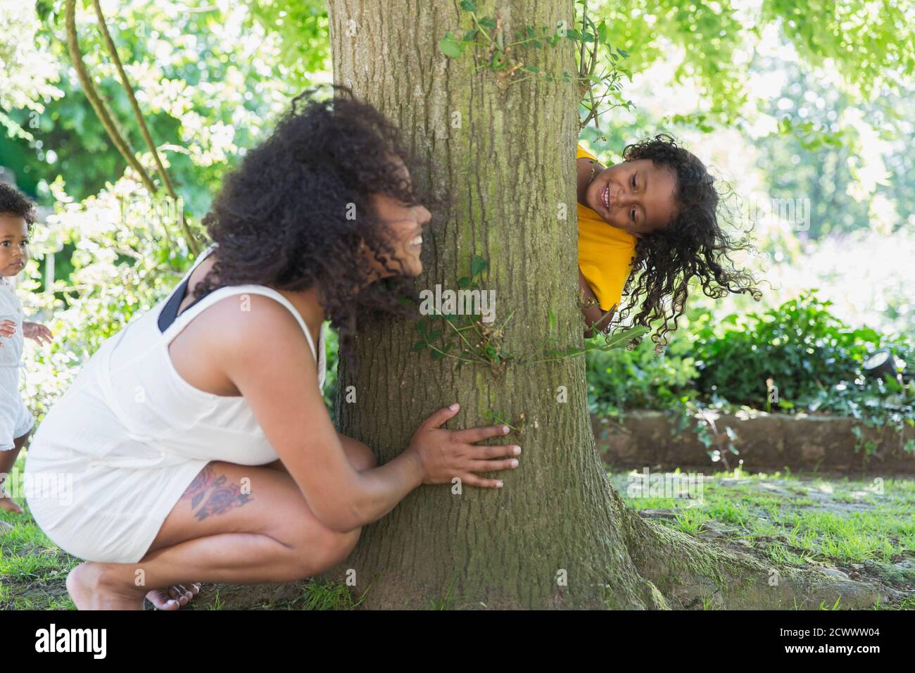 La madre e la figlia giocosa che giocano nascondono e vanno cercano a. albero Foto Stock
