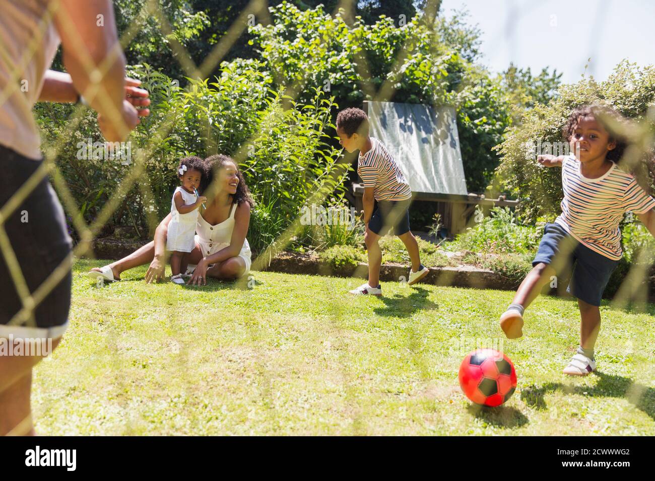 Buona famiglia che gioca a calcio nel soleggiato cortile estivo Foto Stock