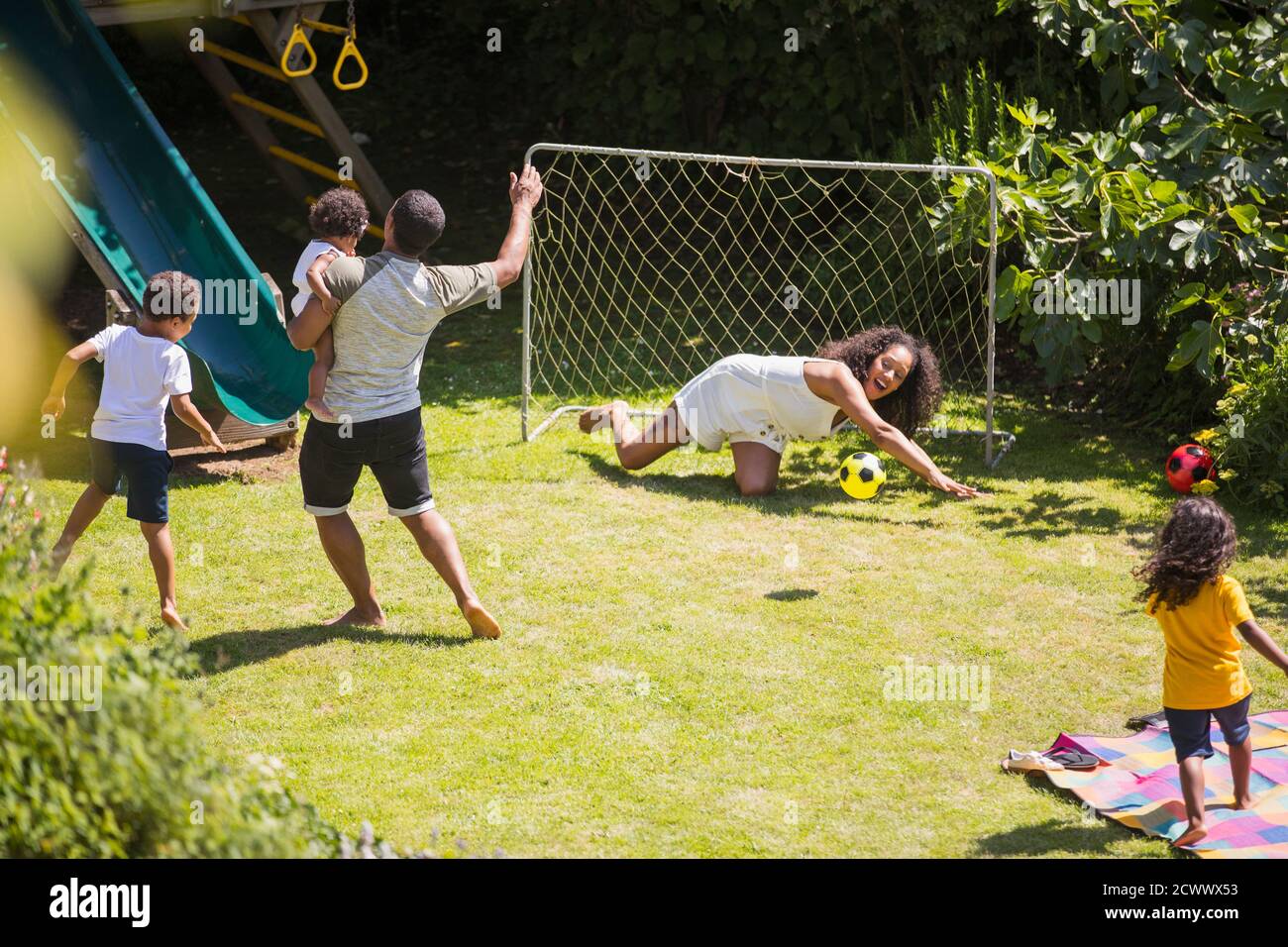 Buona famiglia che gioca a calcio nel soleggiato cortile estivo Foto Stock