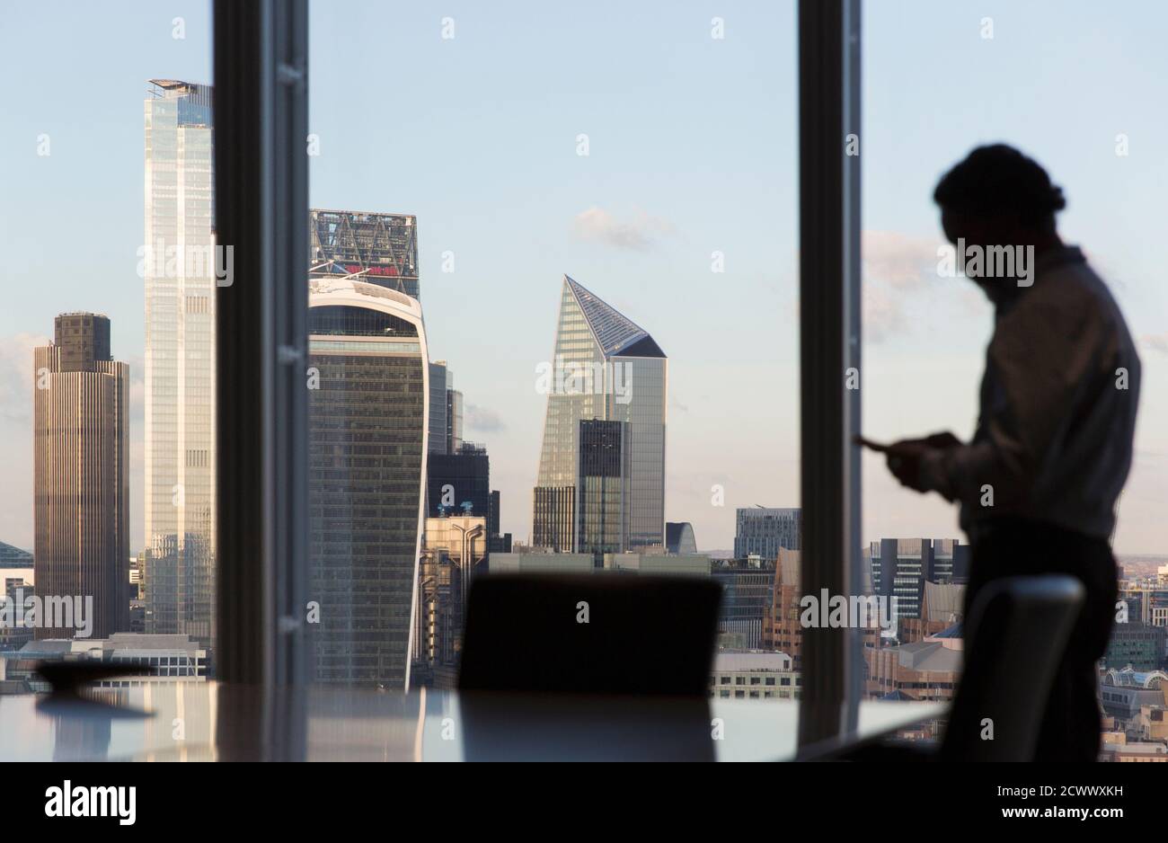 Uomo d'affari che usa lo smartphone alla finestra dell'ufficio di Highrise, Londra, Regno Unito Foto Stock