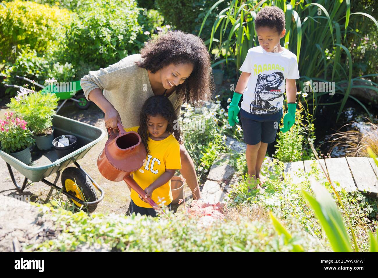 Felice madre e bambini annaffiatura piante in giardino estivo soleggiato Foto Stock