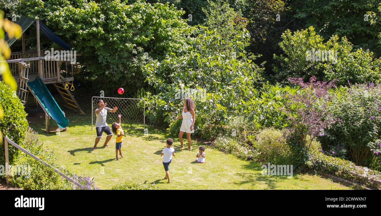 Famiglia che gioca a calcio nel soleggiato cortile estivo Foto Stock