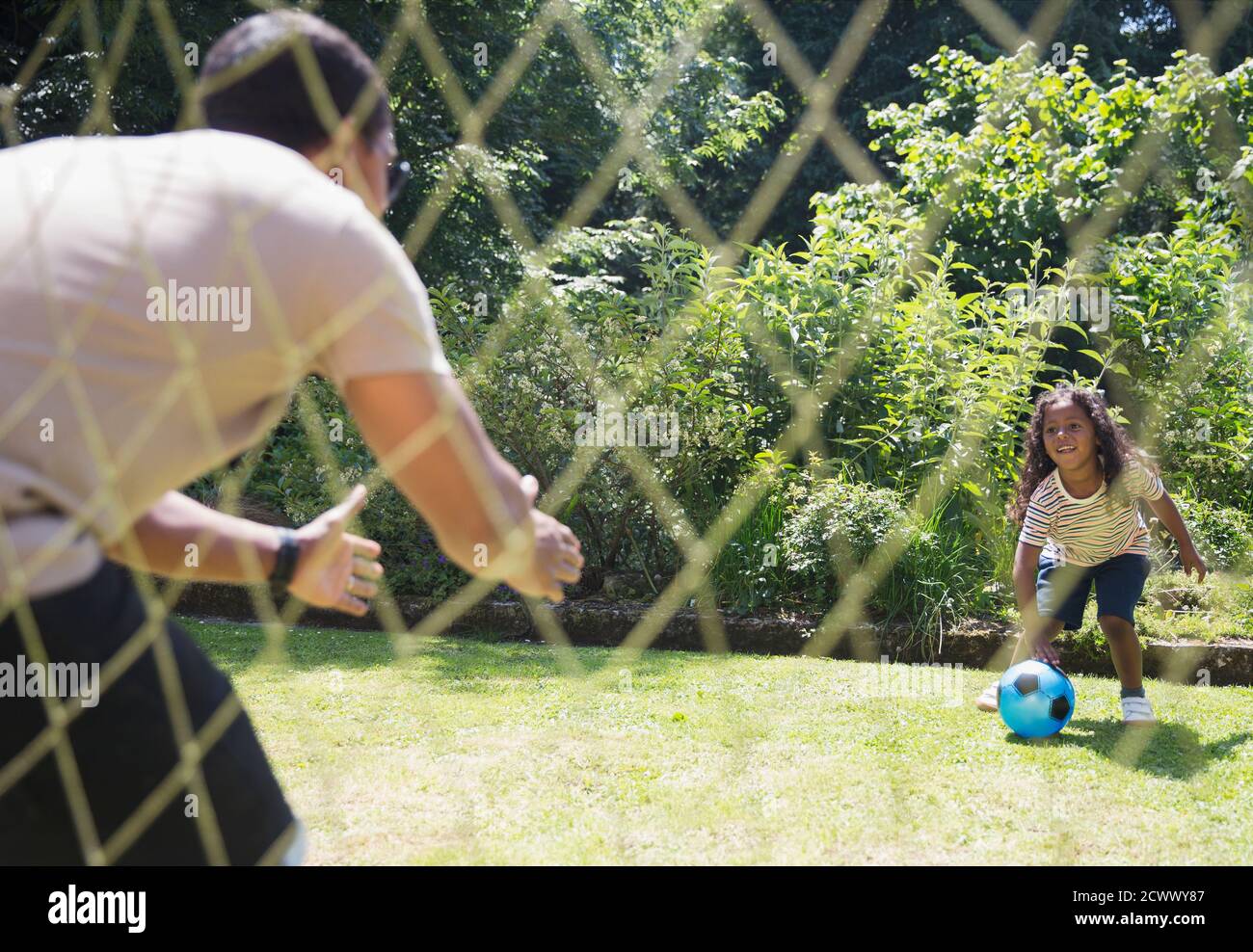 Padre e figlia giocano a calcio nel soleggiato cortile estivo Foto Stock