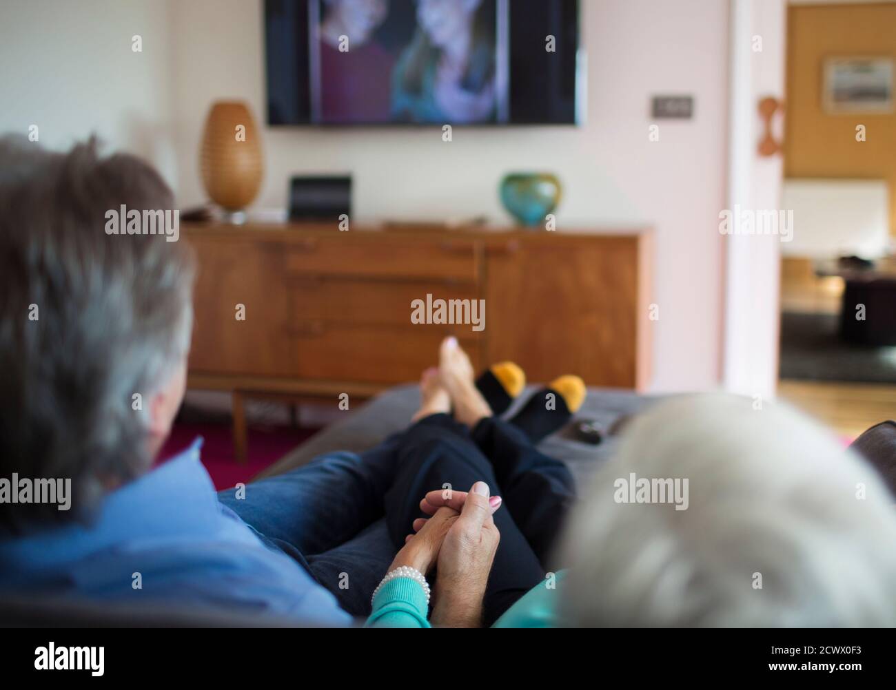 Coppia senior che tiene le mani e guarda la TV sul soggiorno divano Foto Stock