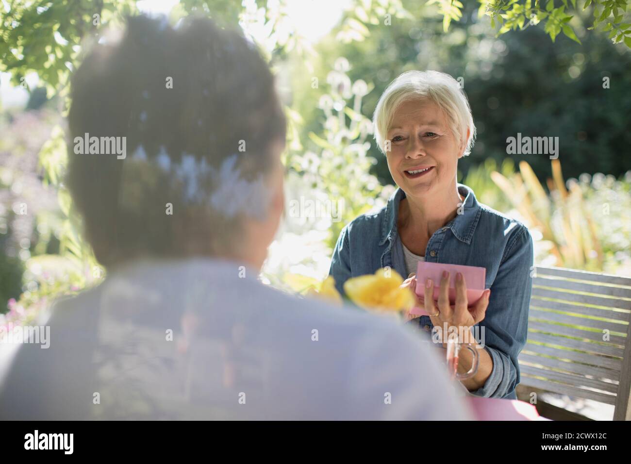 Felice donna anziana regalo di apertura da marito in estate soleggiato patio Foto Stock