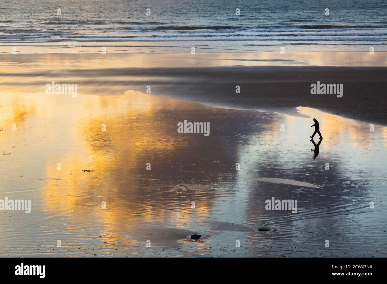 Un uomo dalla silhouette cammina intenzionalmente attraverso una spiaggia vuota a. tramonto Foto Stock