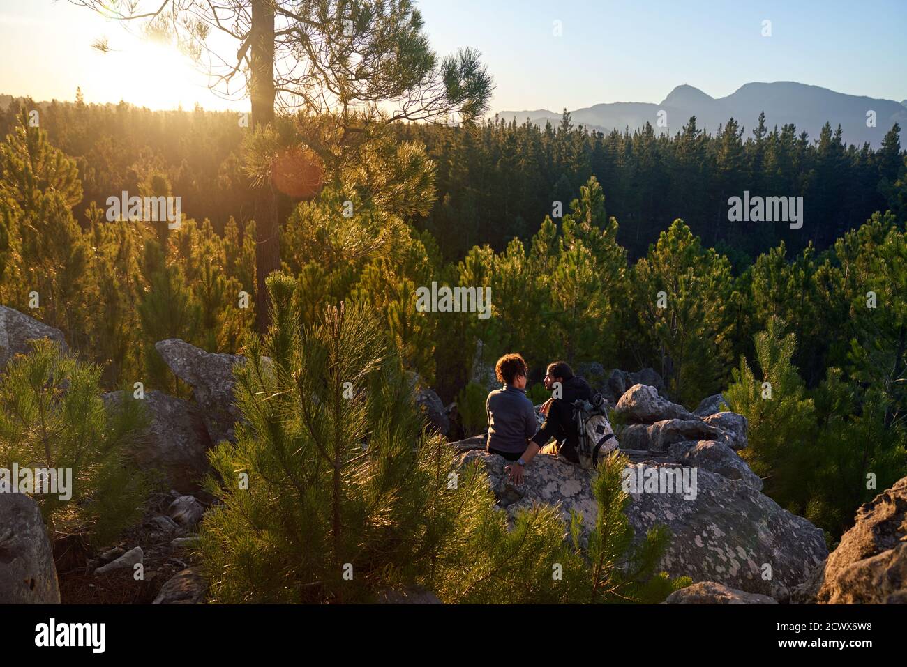 Giovane coppia escursionistica rilassante sulla roccia in boschi soleggiati e panoramici Foto Stock