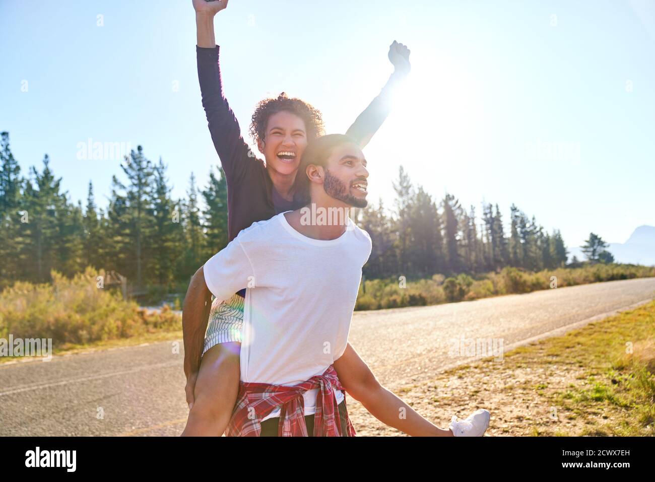 Ritratto Carefree giovane coppia piggybacking al soleggiato a distanza strada Foto Stock