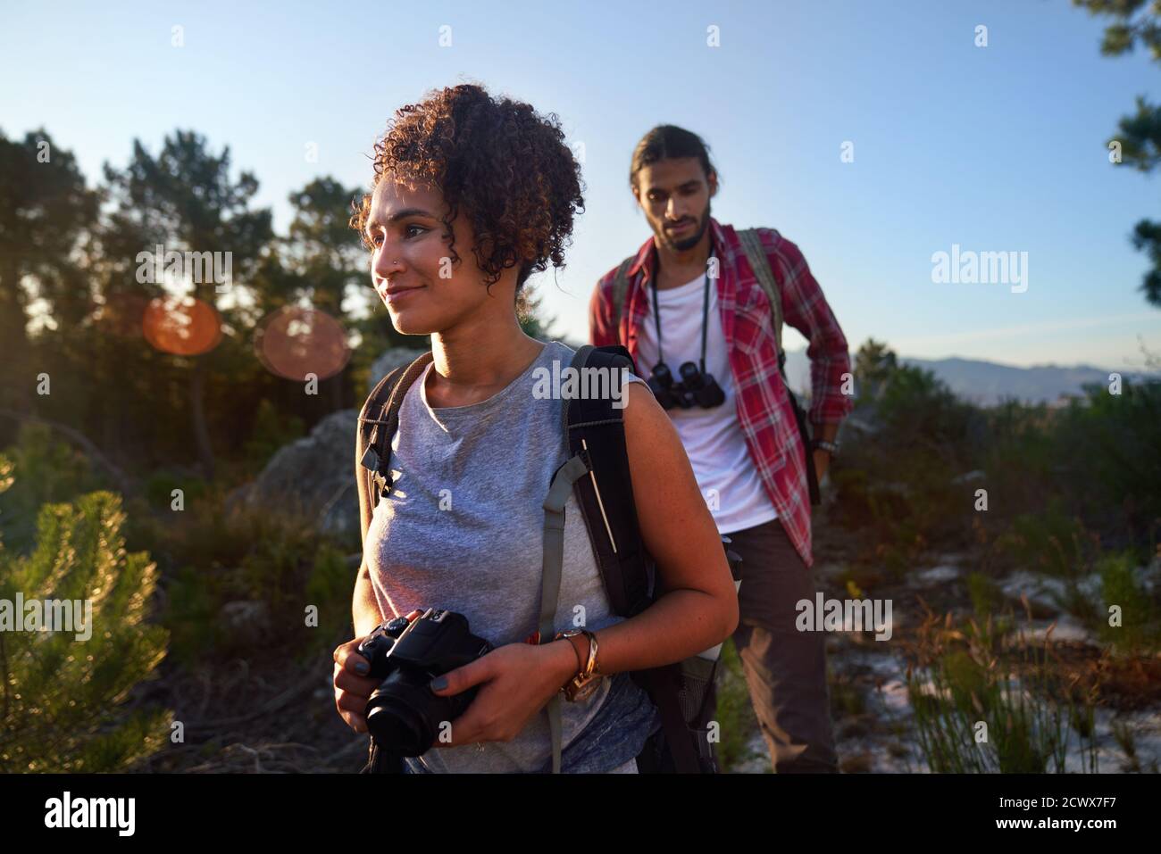 Giovane coppia trekking con macchina fotografica e binocolo in natura soleggiata Foto Stock