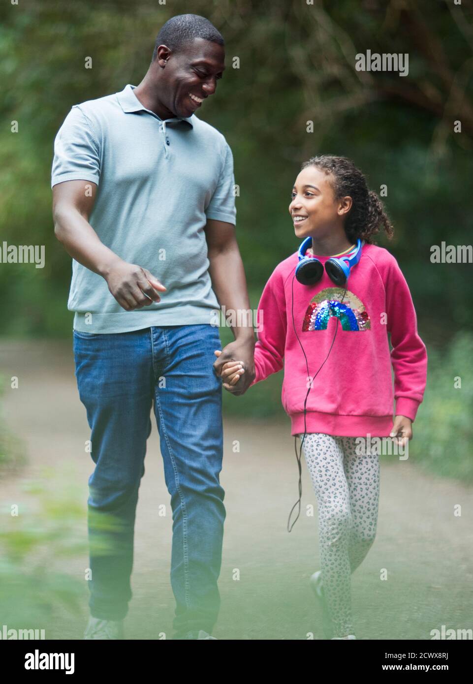 Felice padre e figlia che tengono le mani camminando sul sentiero del parco Foto Stock