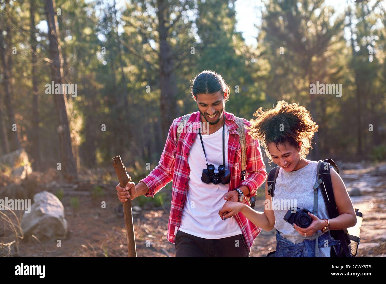 Felice giovane coppia trekking con binocolo e macchina fotografica in sole boschi Foto Stock