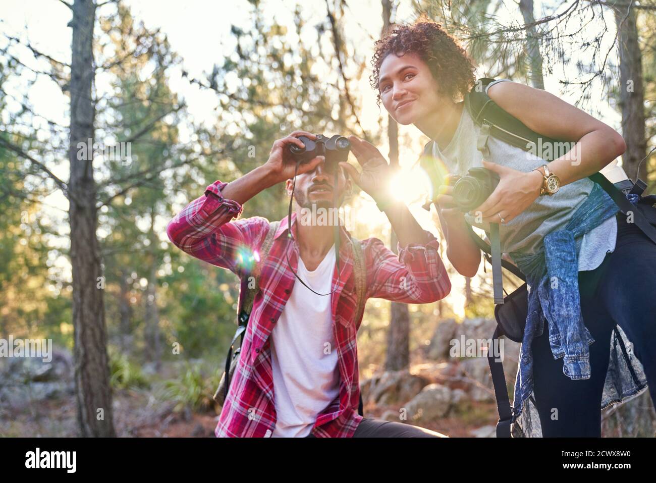 Curiosa giovane coppia escursionista che usa binocoli e fotocamera in sole boschi Foto Stock