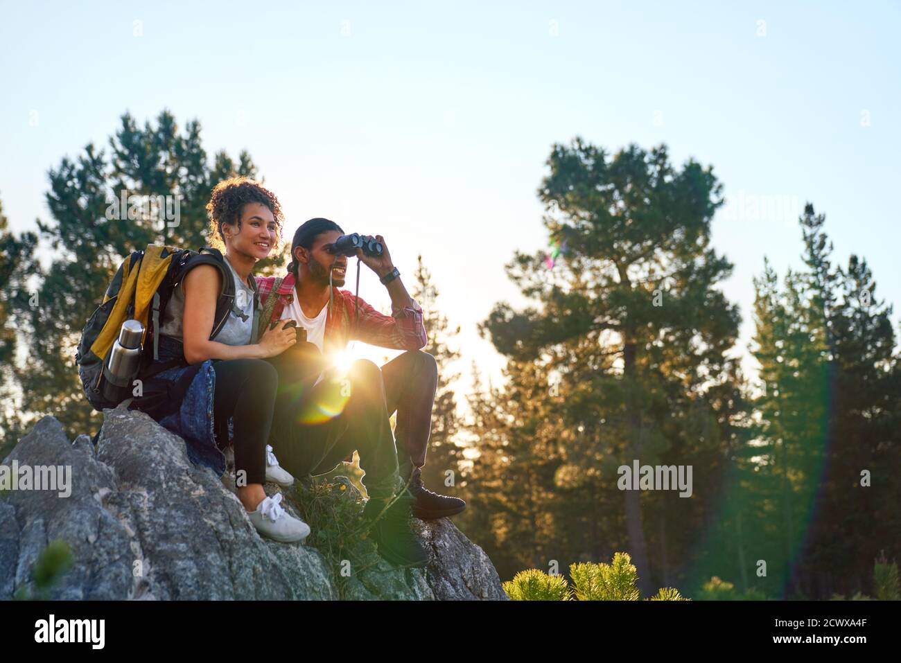 Giovane coppia trekking con binocoli su rocce in boschi soleggiati Foto Stock