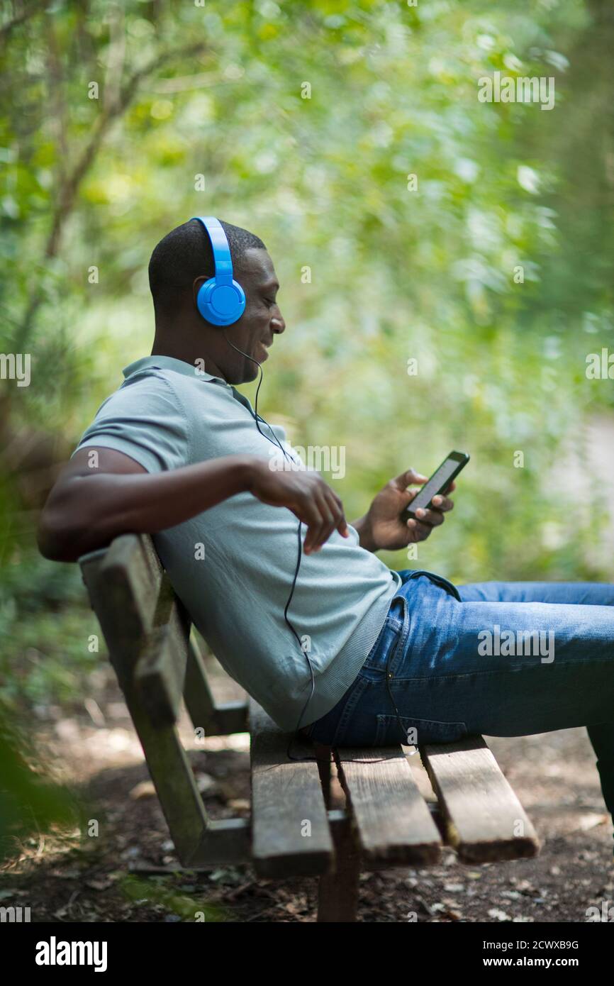 Uomo che ascolta la musica con le cuffie e lo smartphone acceso panca di parcheggio Foto Stock